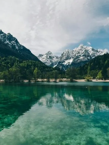 A photo of a turquoise alpine lake with snow-capped mountains and forest in the background